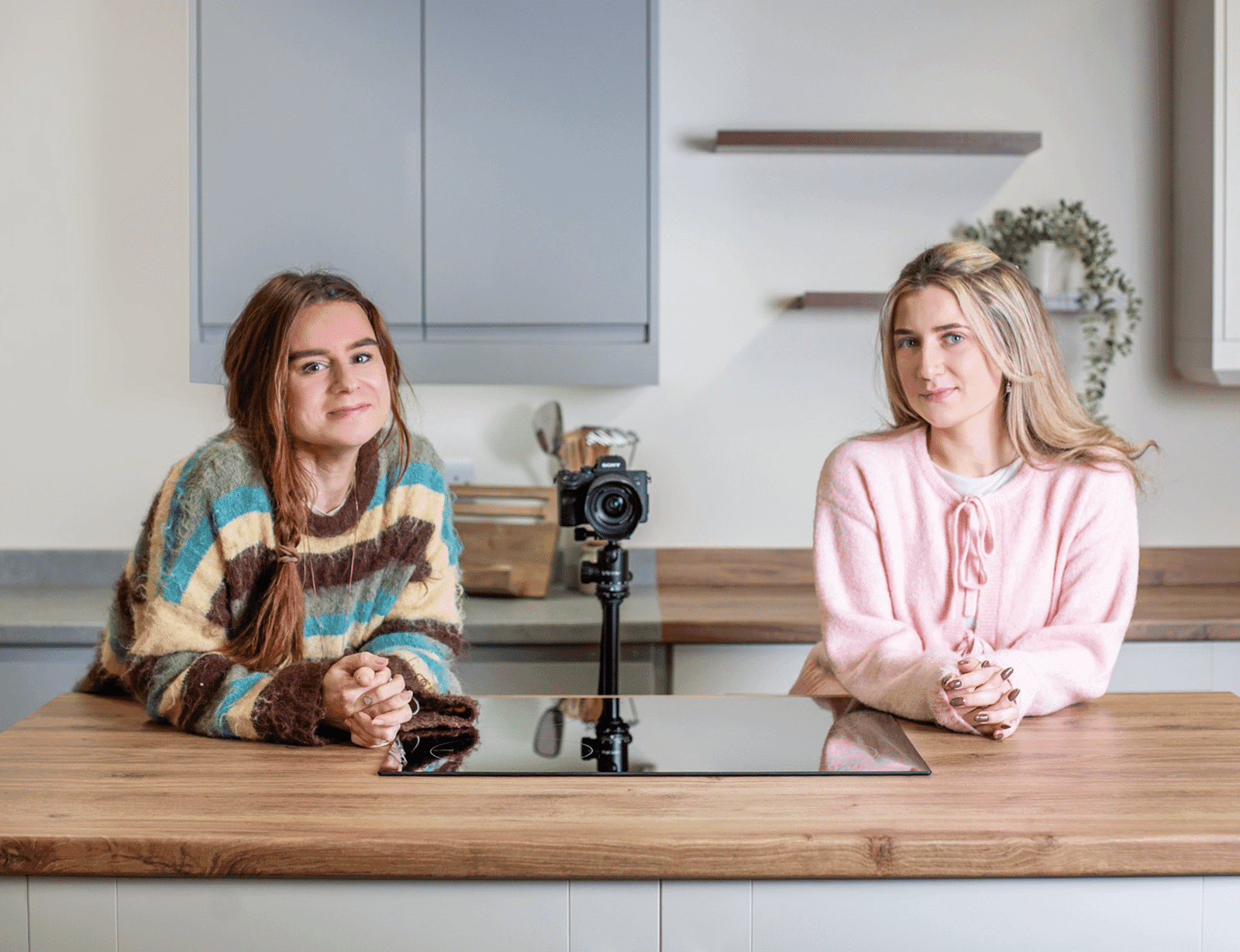Two people sitting at a kitchen counter with a camera on a tripod, ready to film