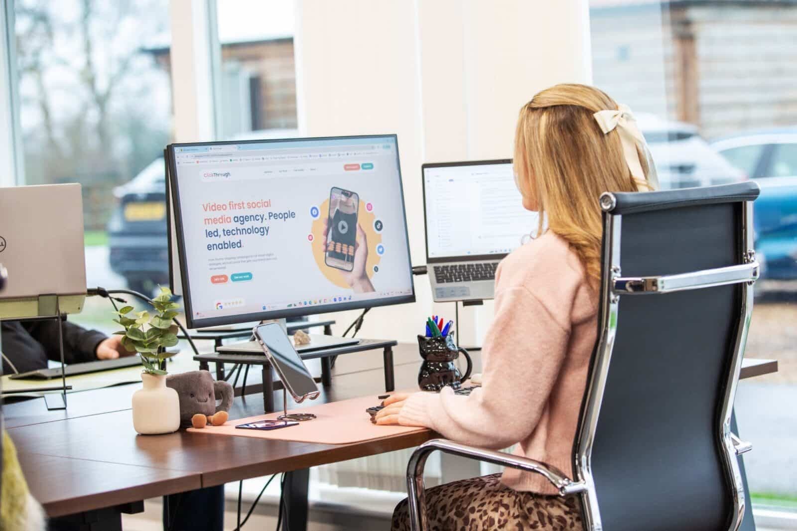 A woman working at a desk with a website open on her monitor