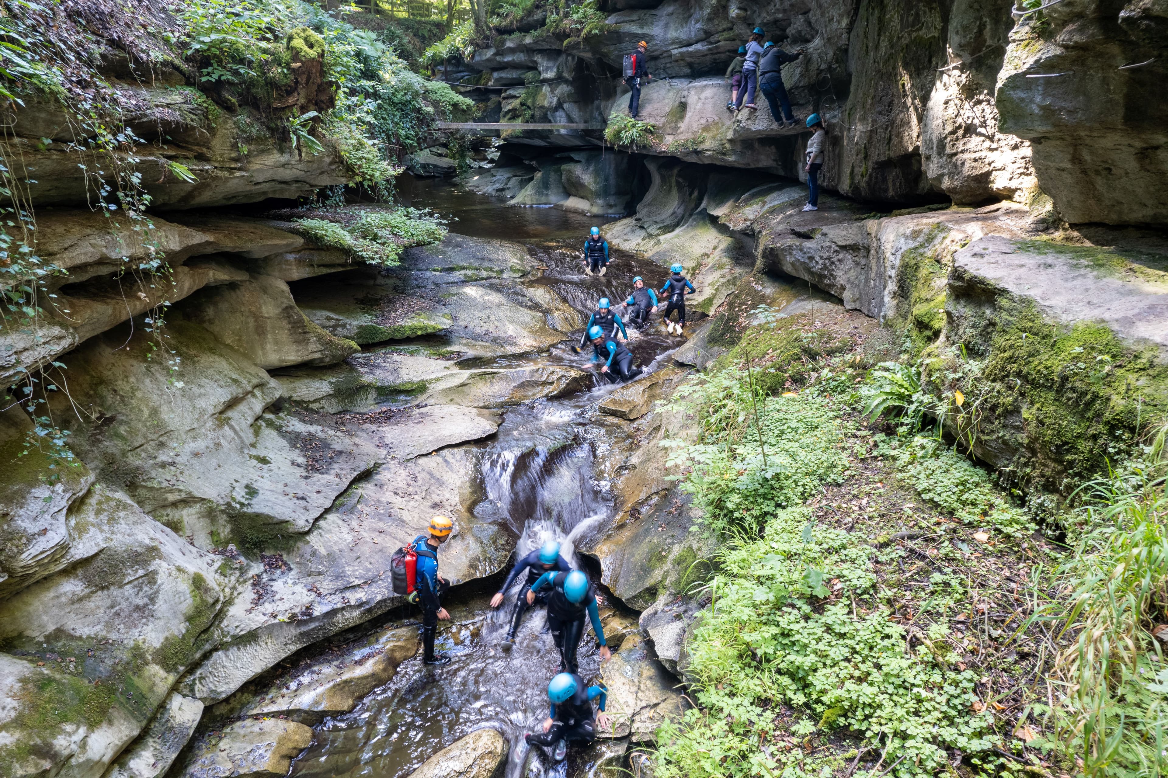 Gorge walkers in helmets making their way along a rocky river gorge
