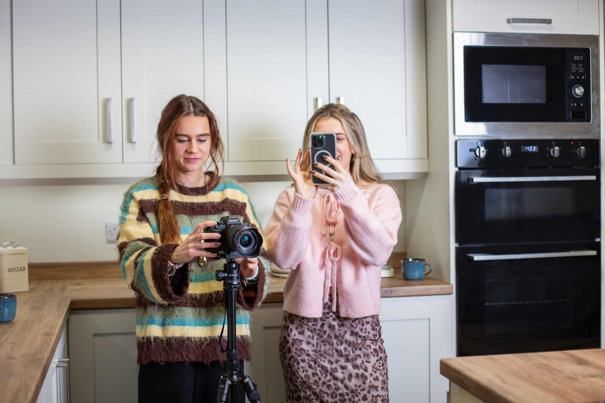 Two people filming in a kitchen, one with a camera and one with a phone