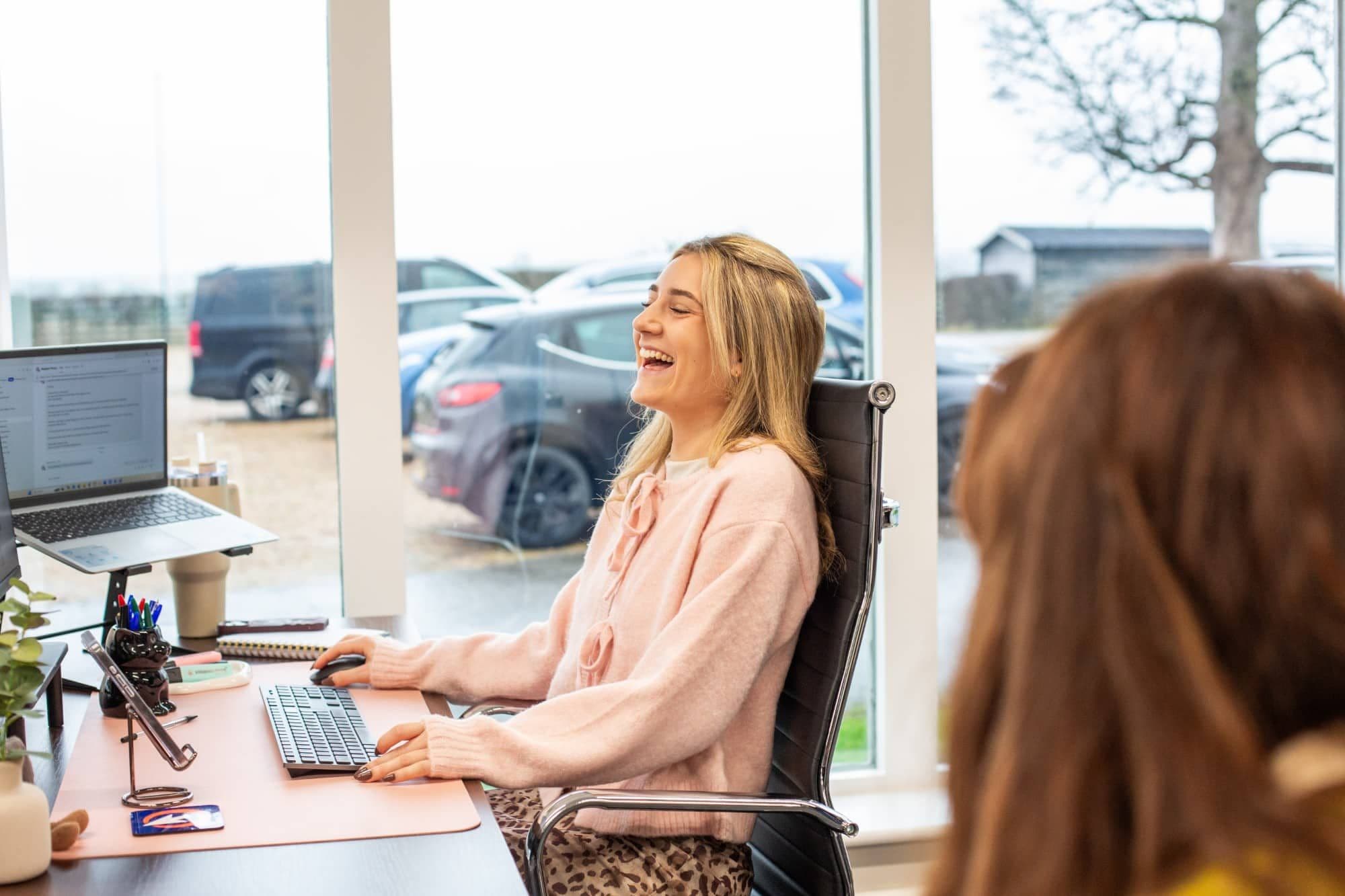 A woman laughing at her desk in a bright office