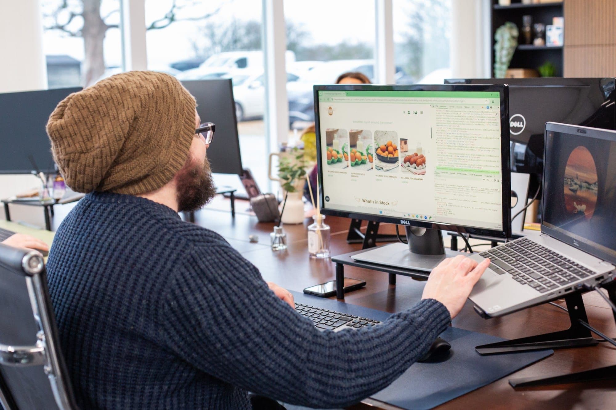 A man in a woolly hat working on a food website at his desk