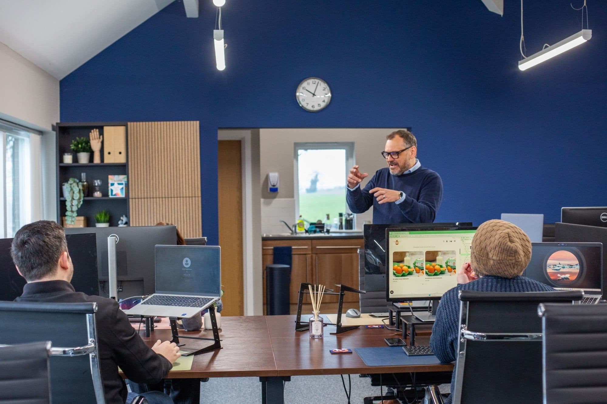 A man presenting to a small group in an office with a navy wall
