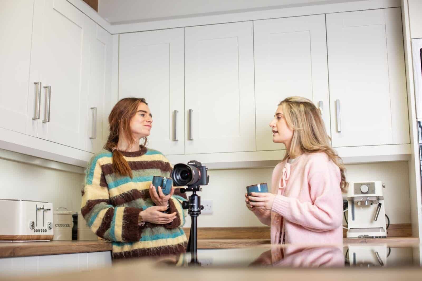 Two people chatting over mugs in a kitchen, filmed on a camera on a tripod