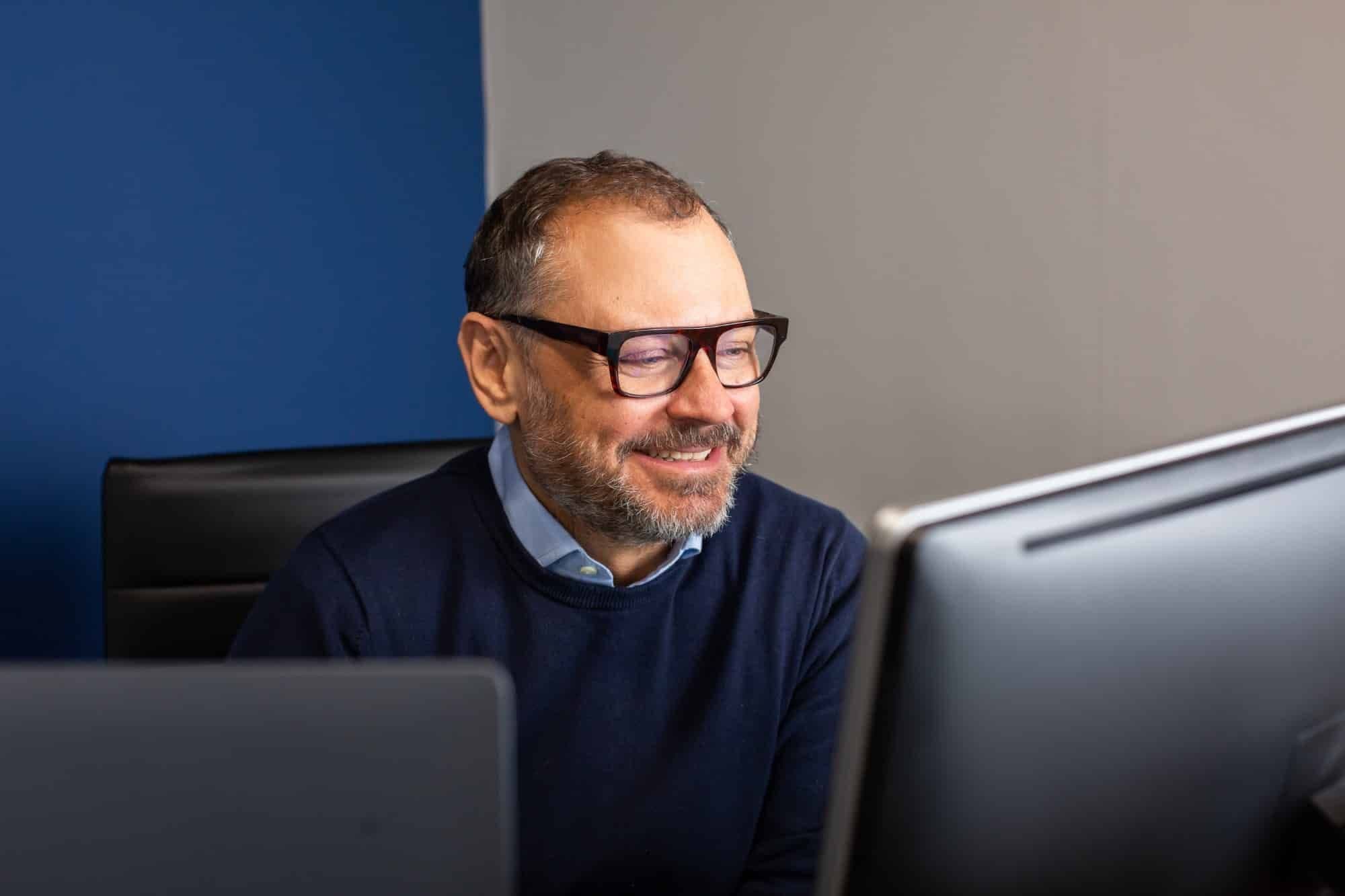 A man in glasses smiling at his computer screen