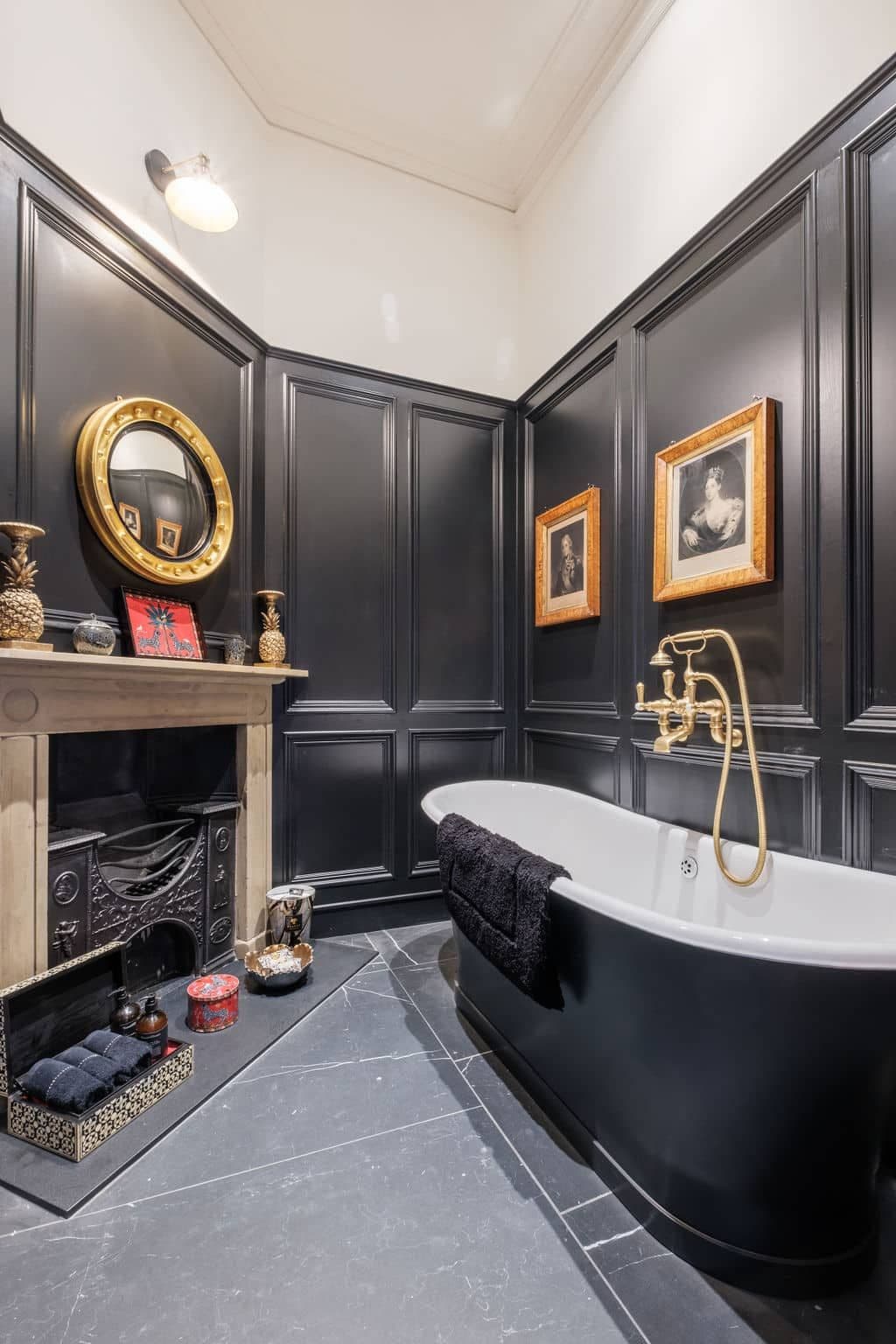 Bathroom with dark panelled walls, a roll-top bath and gold taps